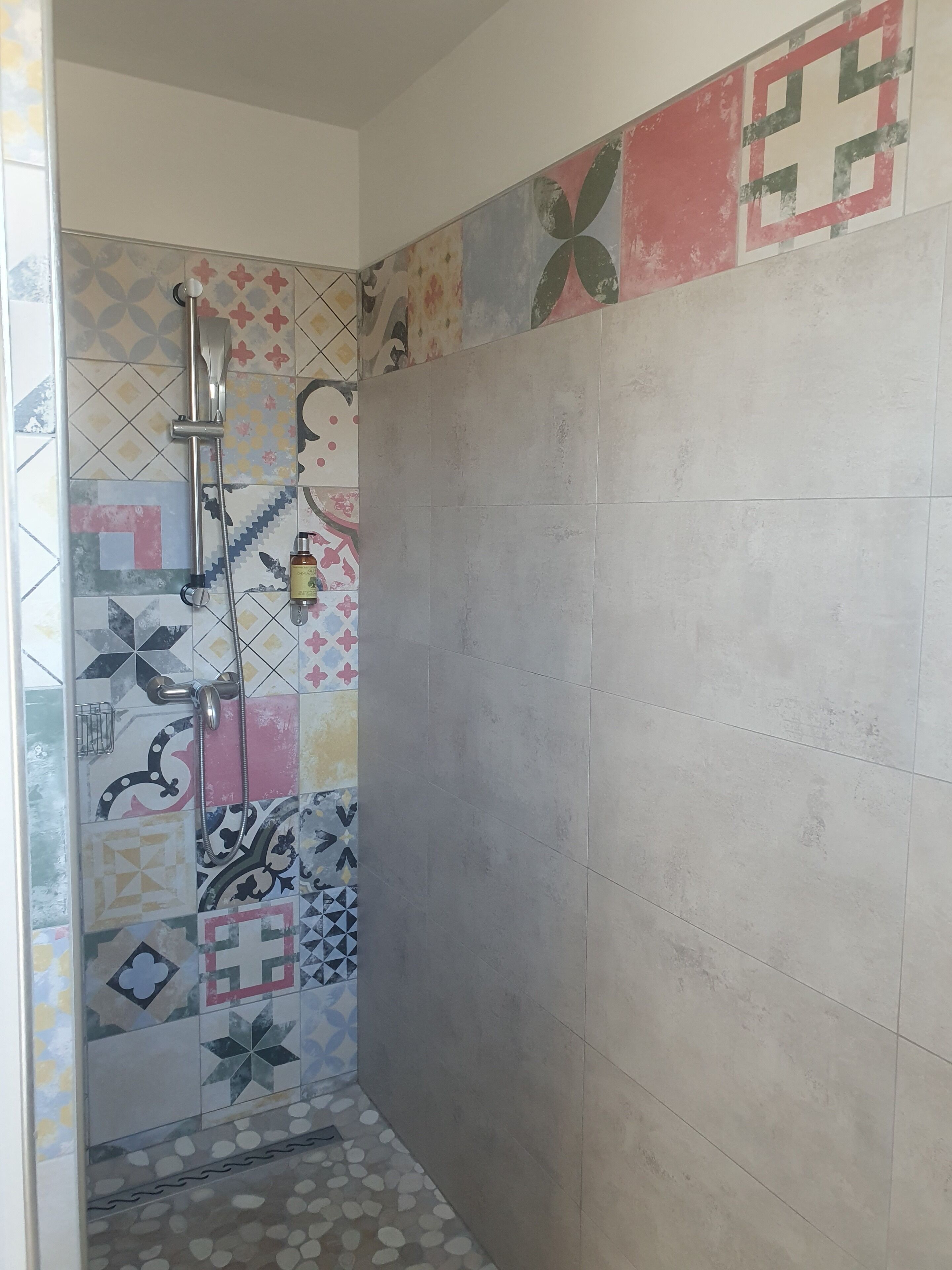 Zona de ducha con pared revestida de azulejos con distintos diseños y suelo de baldosas lisas.