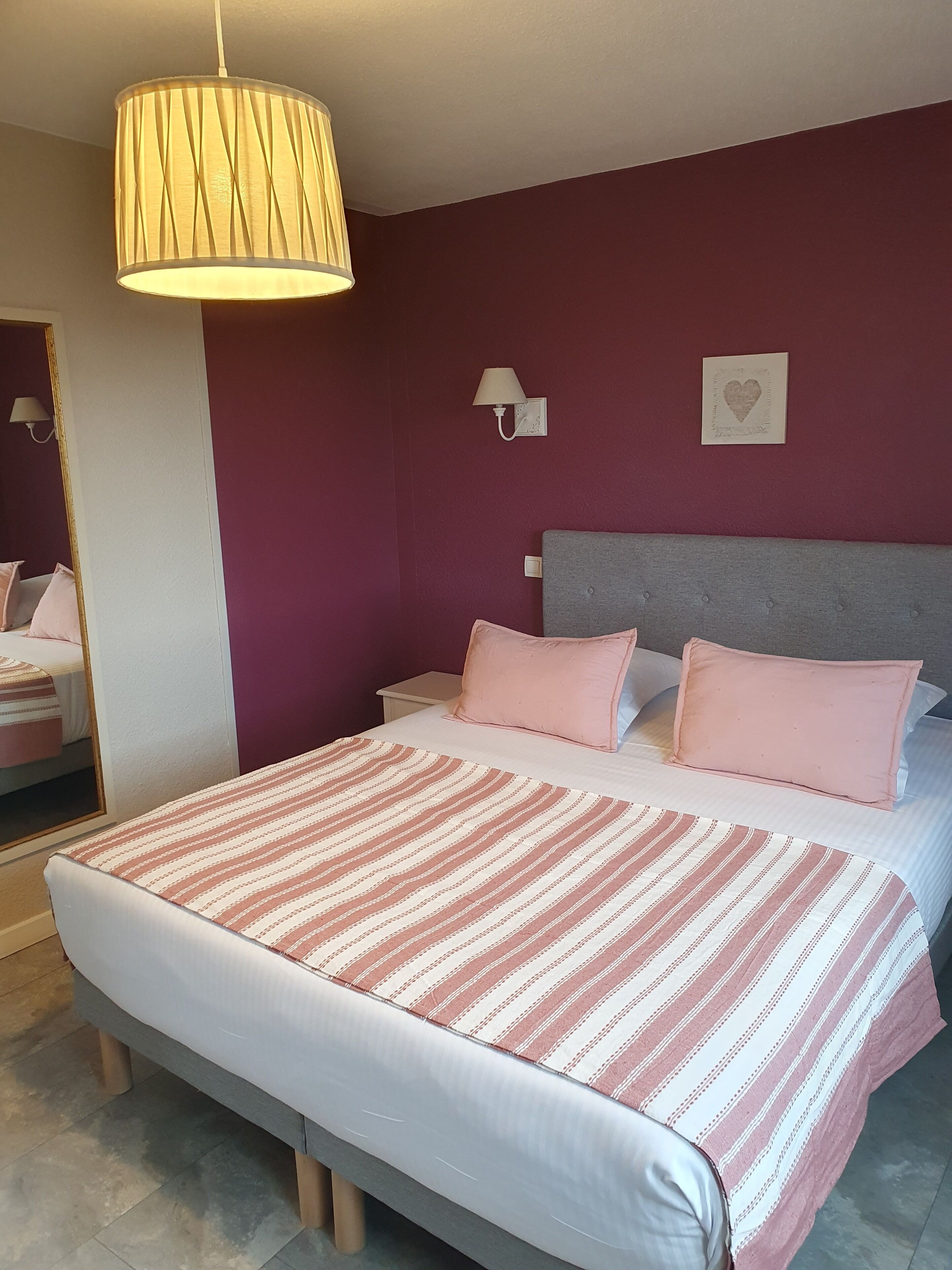 Un dormitorio con cama, lámpara de mesita de noche, luz de pared y decoración con forma de corazón.