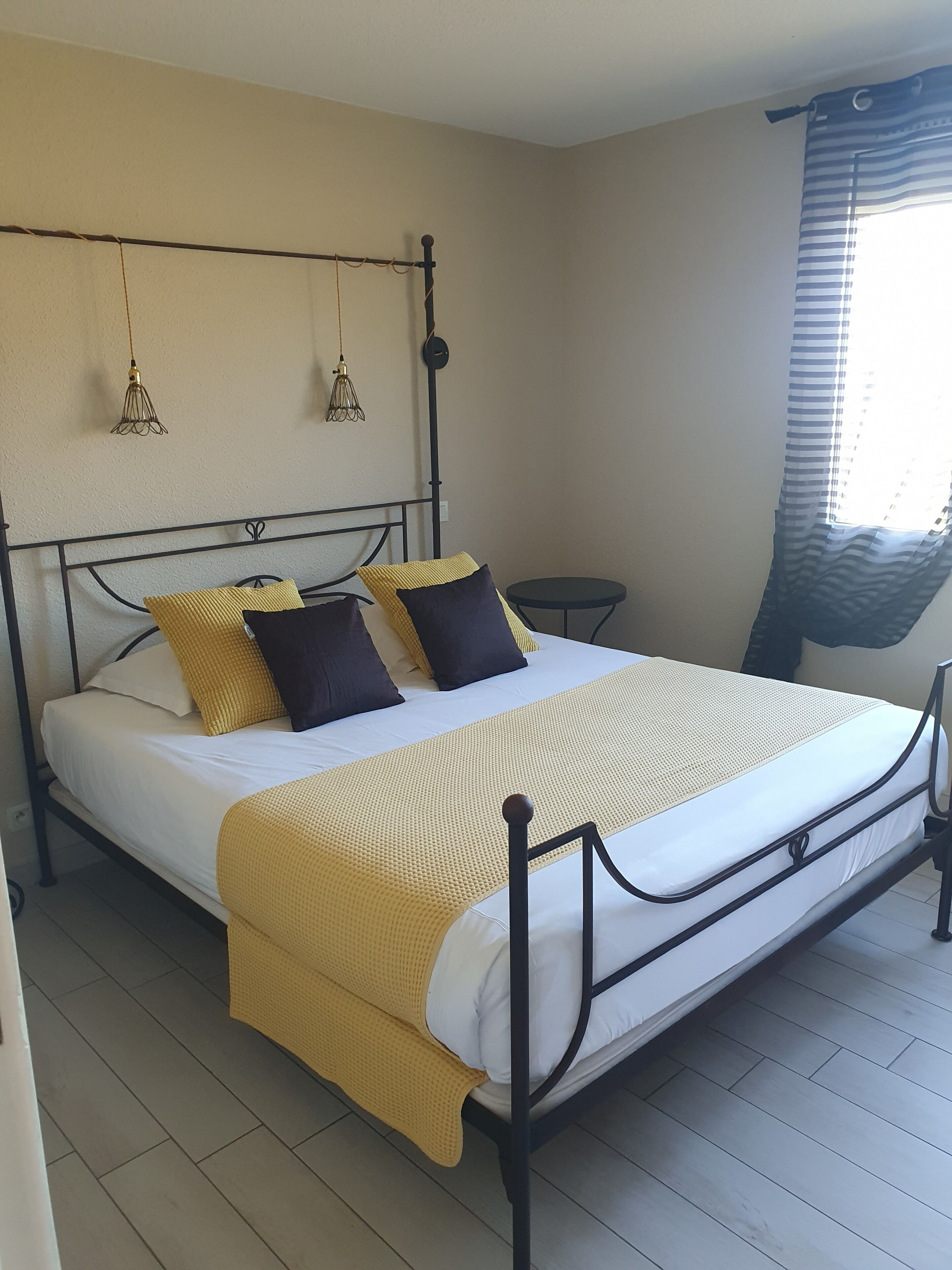 A bed with a metal frame, a yellow blanket, and two pillows. There are two hanging light fixtures on the wall.