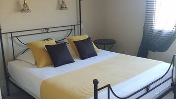 A bed with a metal frame, a yellow blanket, and two pillows. There are two hanging light fixtures on the wall.