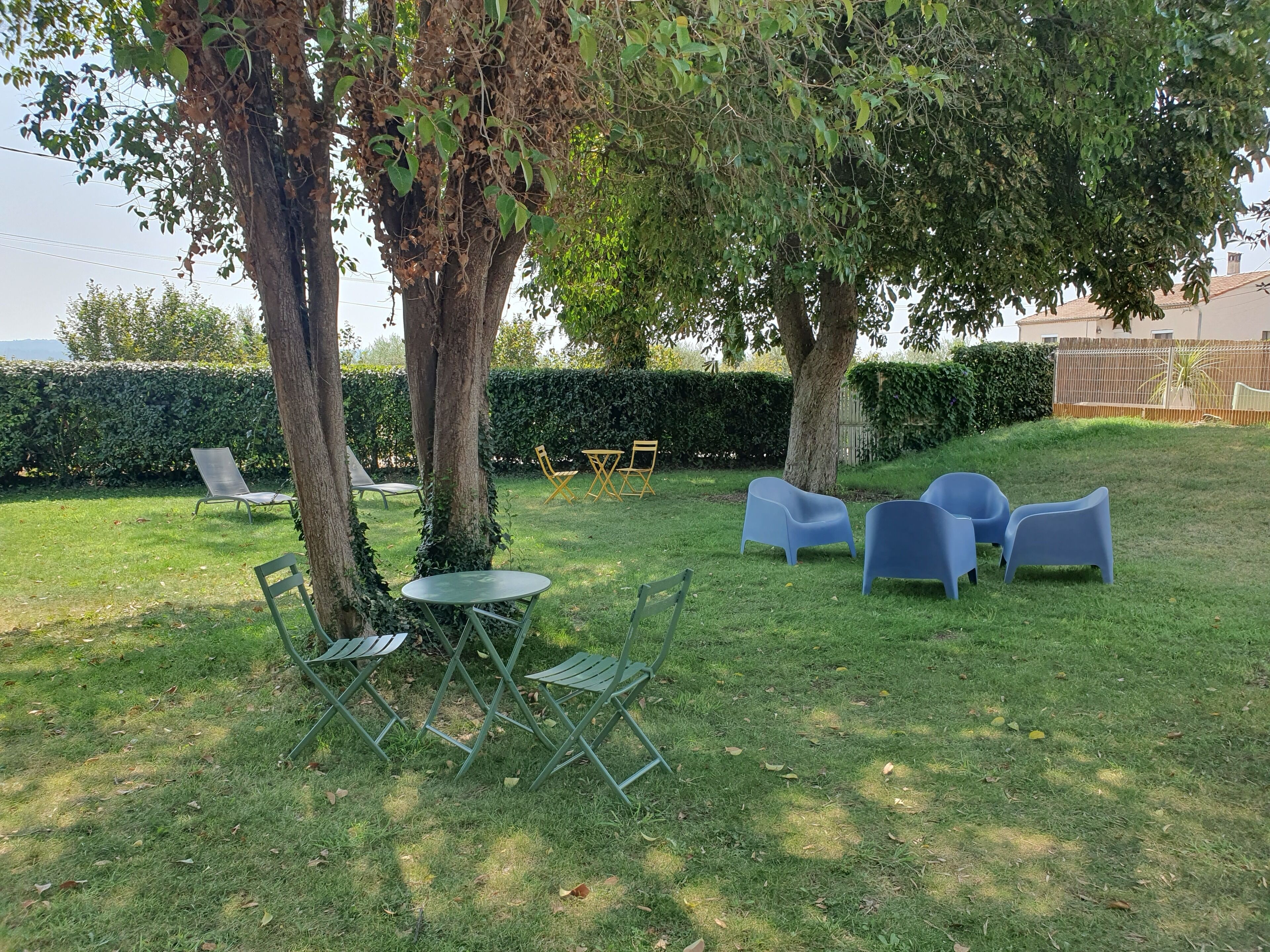 Un espace extérieur aménagé avec une table et des chaises, entouré d’arbres et d’une haie.