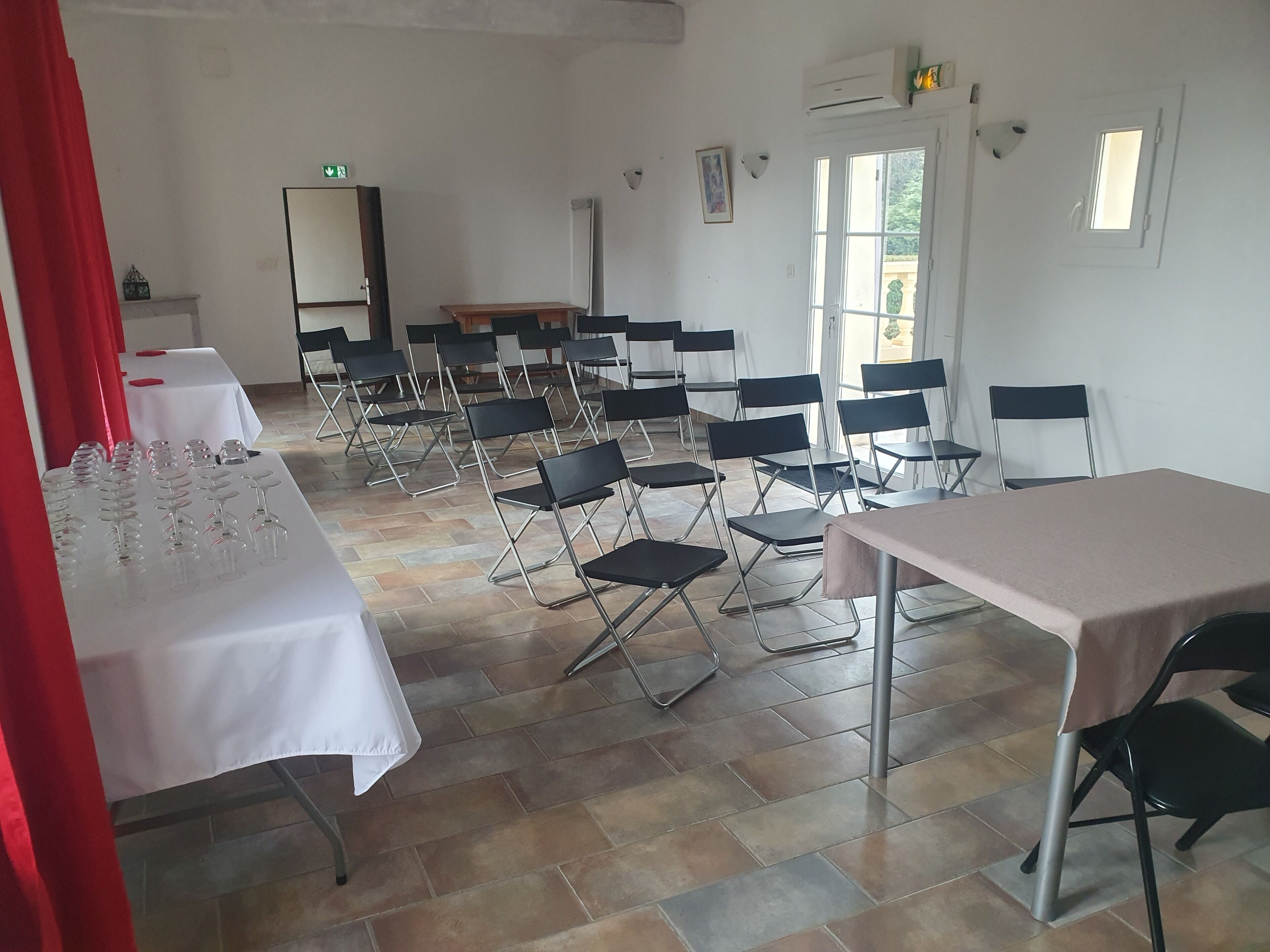 Une salle de conférence équipée de chaises et de tables pliantes, ainsi que d’une table blanche sur laquelle sont disposés des verres à vin.