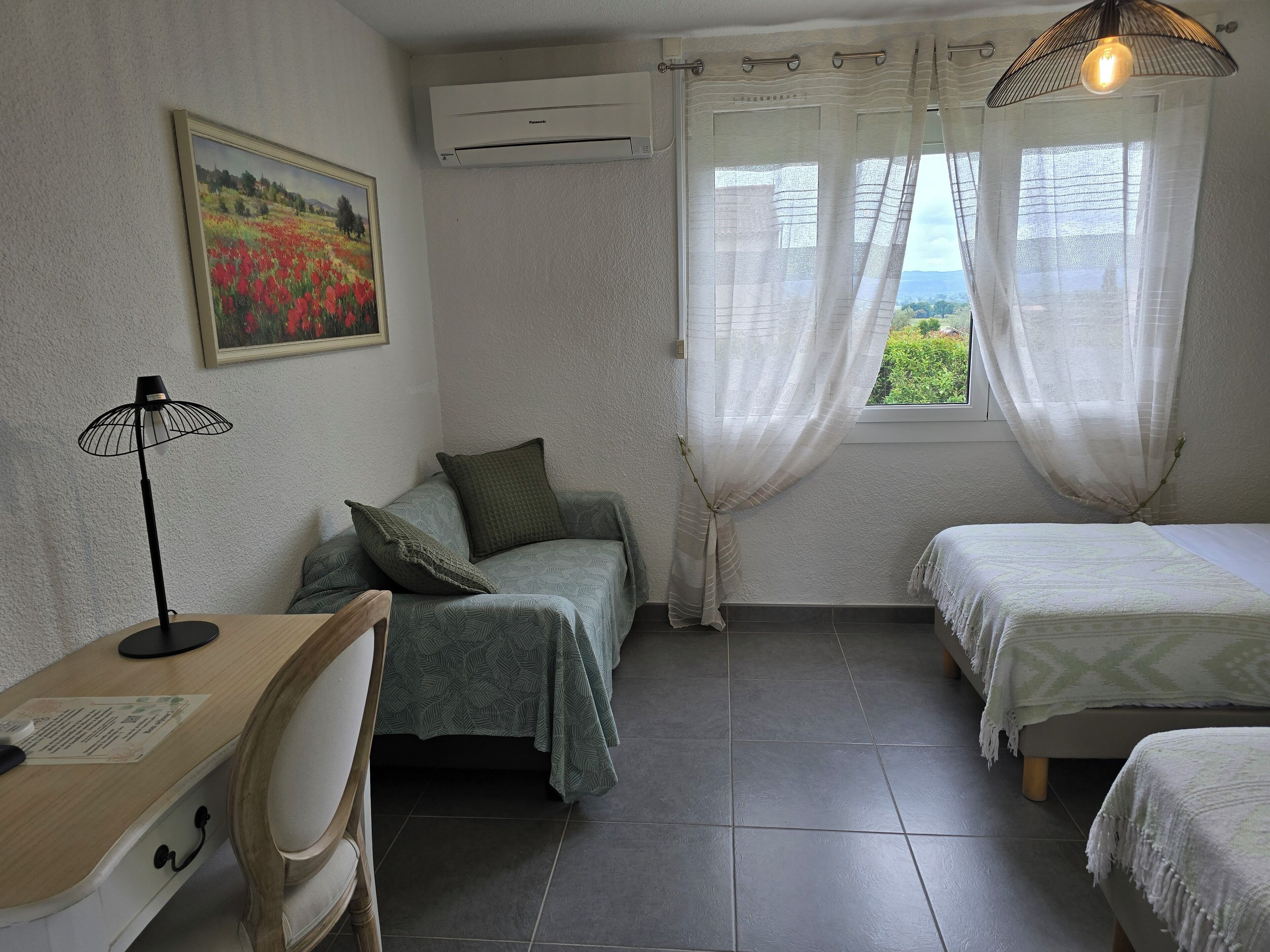 A bedroom with two beds, a desk, a chair, a lamp, and a painting on the wall.