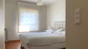 Un dormitorio con una cama, una ventana con persianas, un radiador y un interruptor de luz en la pared.