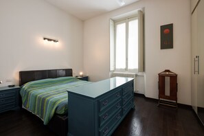 A bedroom with a bed, dresser, nightstand, and a window with blinds. - Flatty Apartments - Stelvio (Milan)