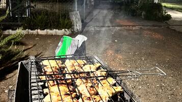 Una parrilla con brochetas de comida, una bolsa verde y una cerca de malla metálica al fondo.