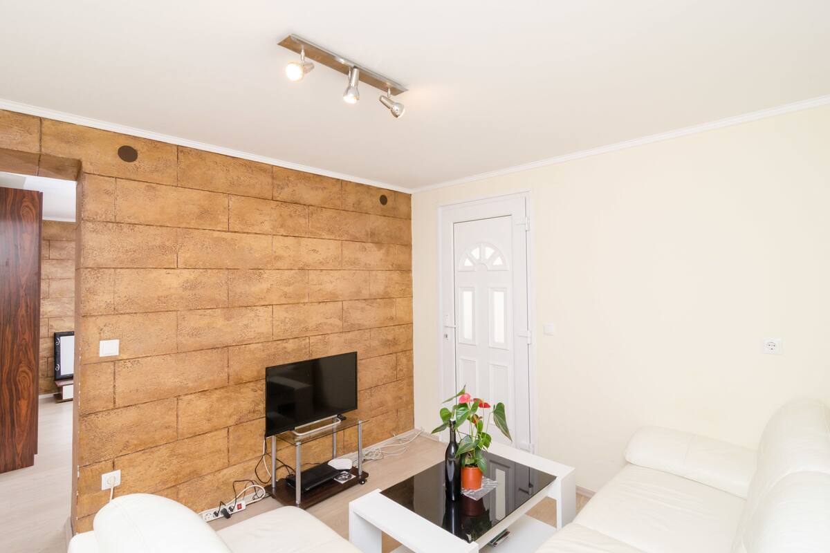 A living room with a brick wall, a flat-screen TV, white sofas, and a coffee table with a plant.