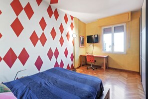 A bedroom with a bed, a desk with a chair, a TV, and a window with blinds. - Flatty Apartments - Transiti (Milan)