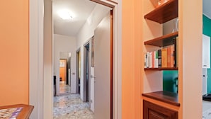 Um corredor com chão de azulejos, estantes de madeira com livros e uma porta que dá para outro aposento.