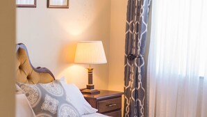 A neatly made bed with a patterned pillow, a bedside lamp, and a framed quote on the wall. - Eden Villas (Harare)