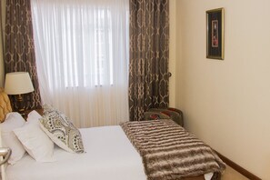 Une chambre d’hôtel avec un lit, une lampe de chevet, un rideau à motifs et un tableau encadré au mur.