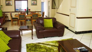 A living room with a brown leather sofa, a wooden coffee table, and a dining area with wooden chairs and a table. - Eden Villas (Harare)