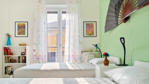 A bedroom with two beds, a bookshelf, a window with curtains, and a wall-mounted fan. - Flatty Apartments - Alserio (Milan)