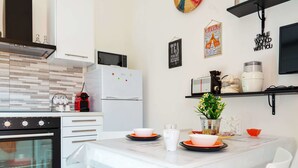 A modern kitchen with white cabinetry, a built-in oven, a microwave, and a refrigerator. There is a dining table set with plates and a vase of flowers. - Flatty Apartments - Alserio (Milan)
