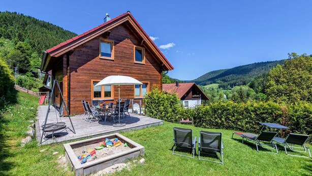 A wooden cabin with a patio, outdoor seating, and a sandbox. - Wellness Ferienhaus Fronwald (Alpirsbach)