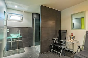 A modern bathroom with a glass sink, a shower, and a small seating area with a table and chairs.