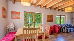 A spacious room with wooden beams, a dining table with chairs, a sofa, and a window with a view of greenery. - Wellness Ferienhaus Fronwald (Alpirsbach)