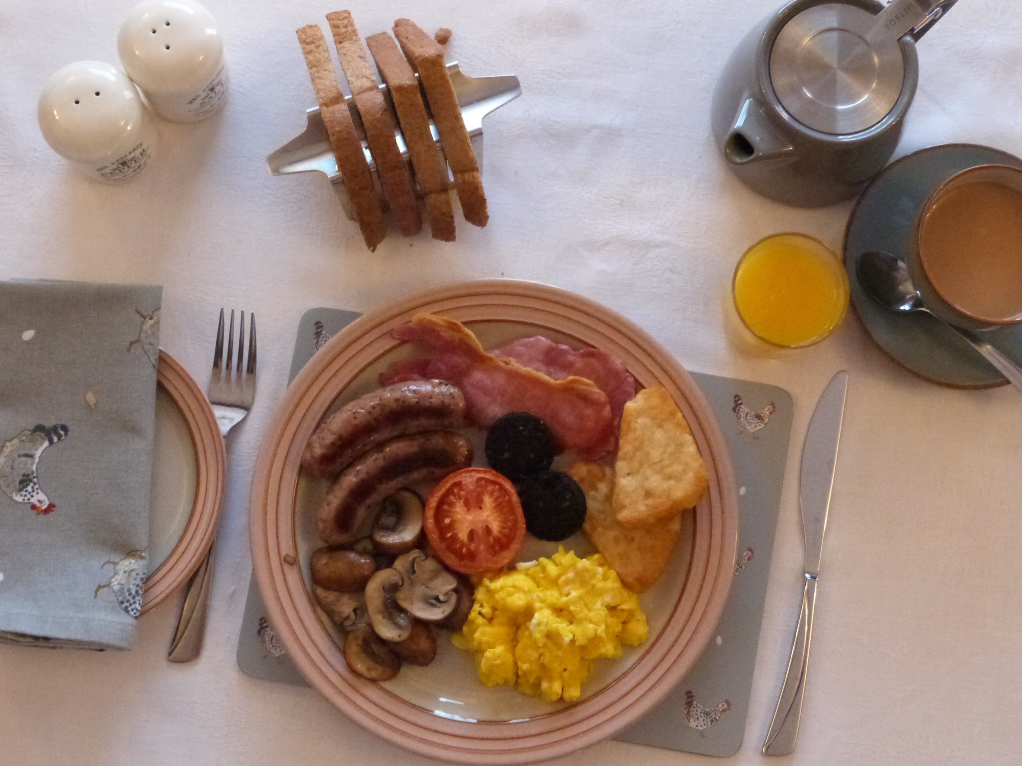 Une assiette de petit-déjeuner comprenant des saucisses, du bacon, des champignons, des œufs brouillés et des toasts.