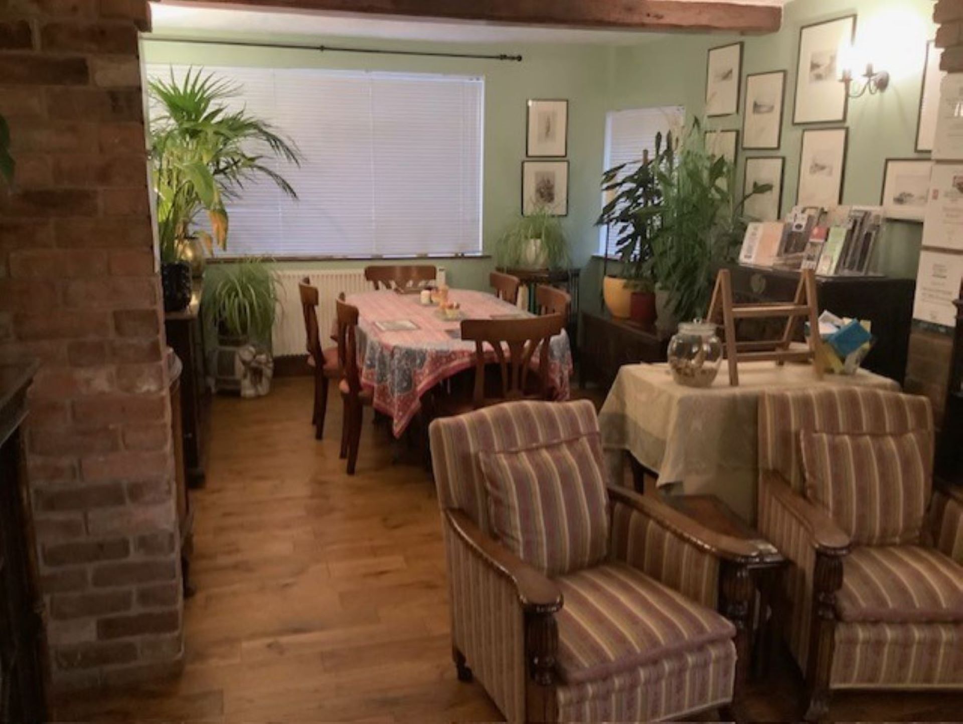 A cozy dining area with a wooden table and chairs, a brick wall, and potted plants.