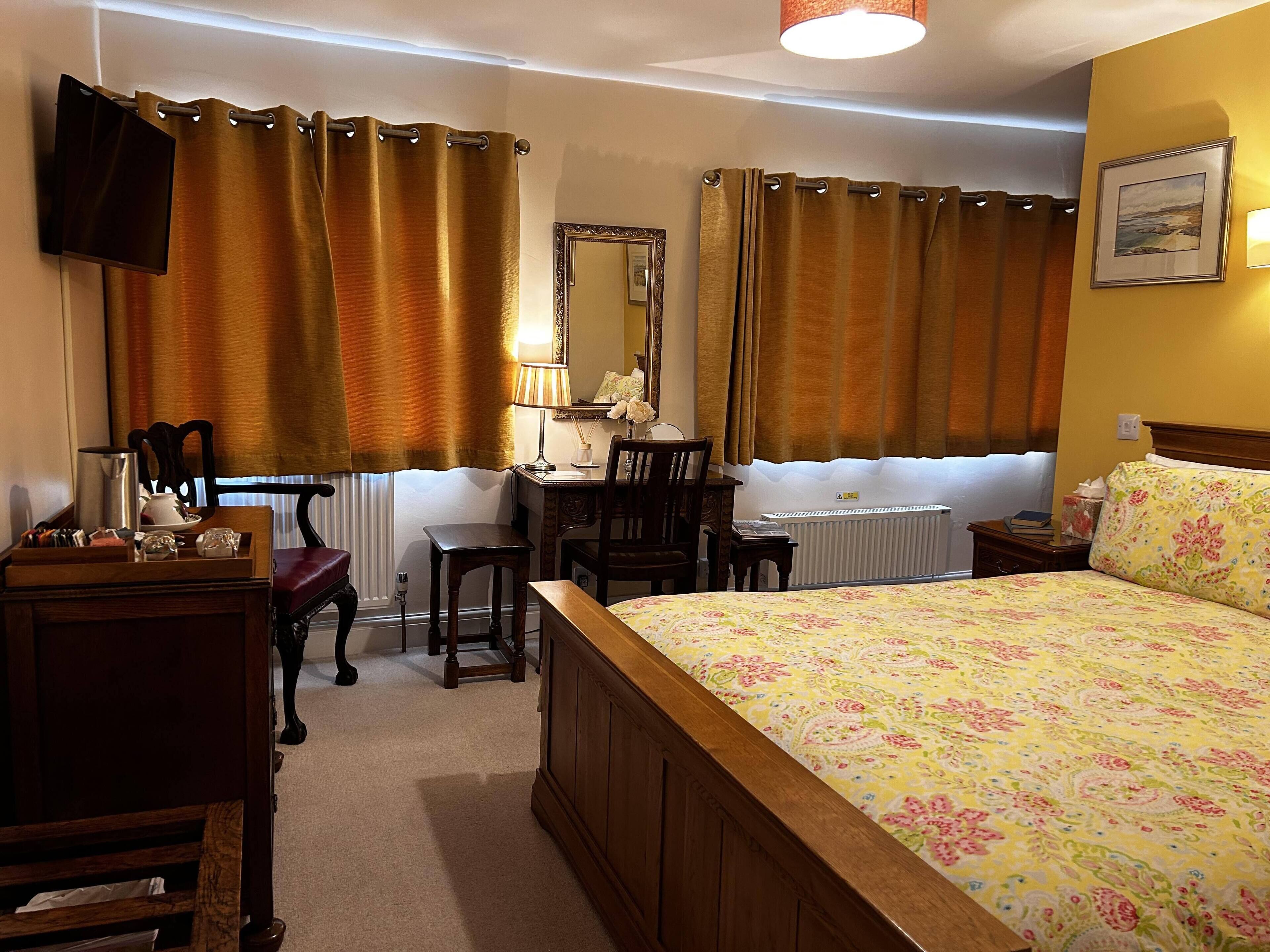 Habitación de hotel con cama, escritorio, silla, espejo, radiador y televisor montado en la pared.