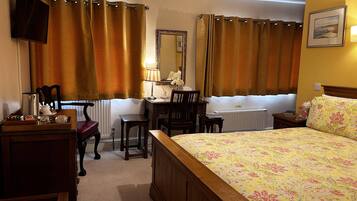 Habitación de hotel con cama, escritorio, silla, espejo, radiador y televisor montado en la pared.