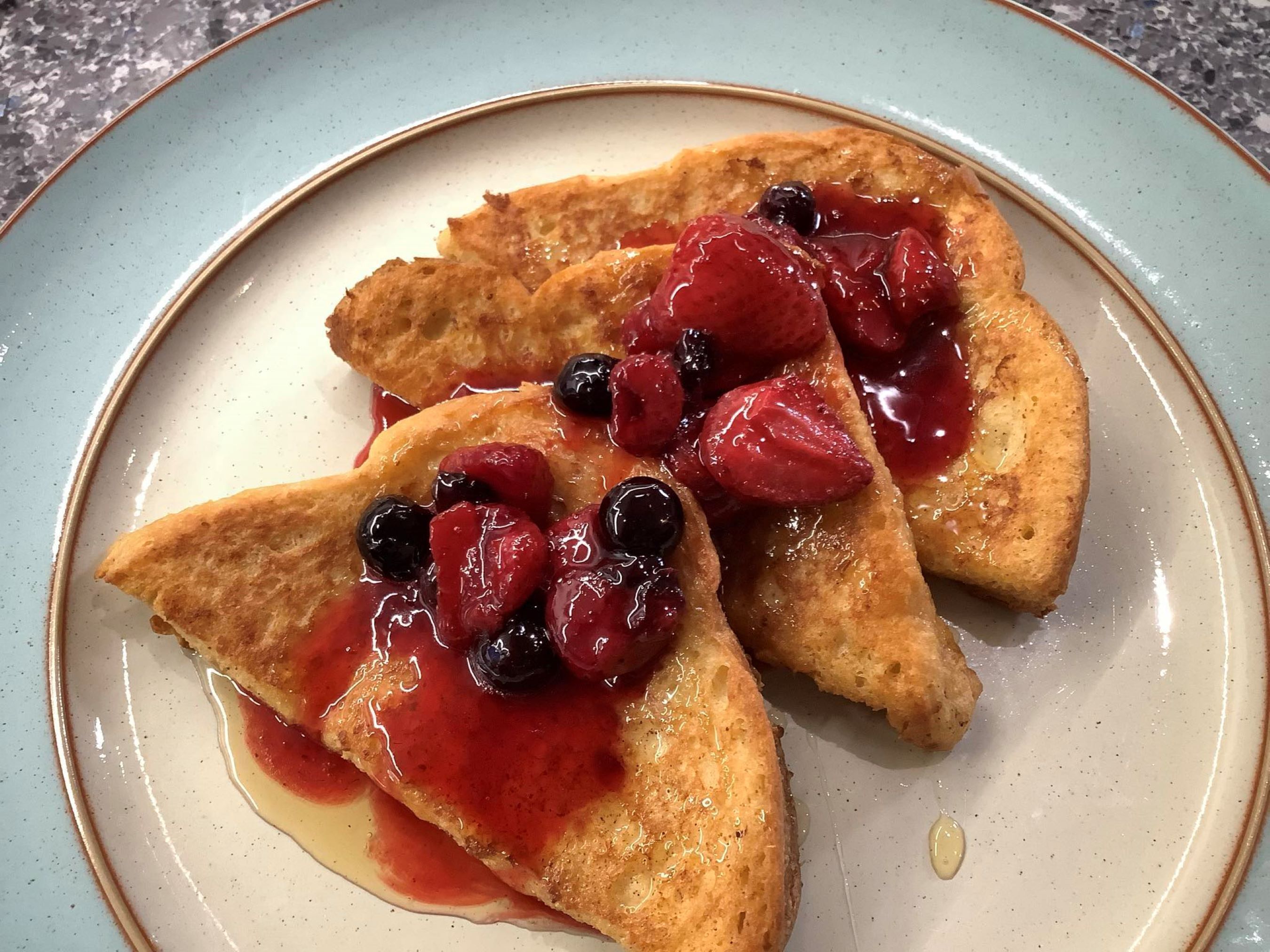 Un plato con tres rebanadas de tostada triangular adornadas con bayas y jarabe.