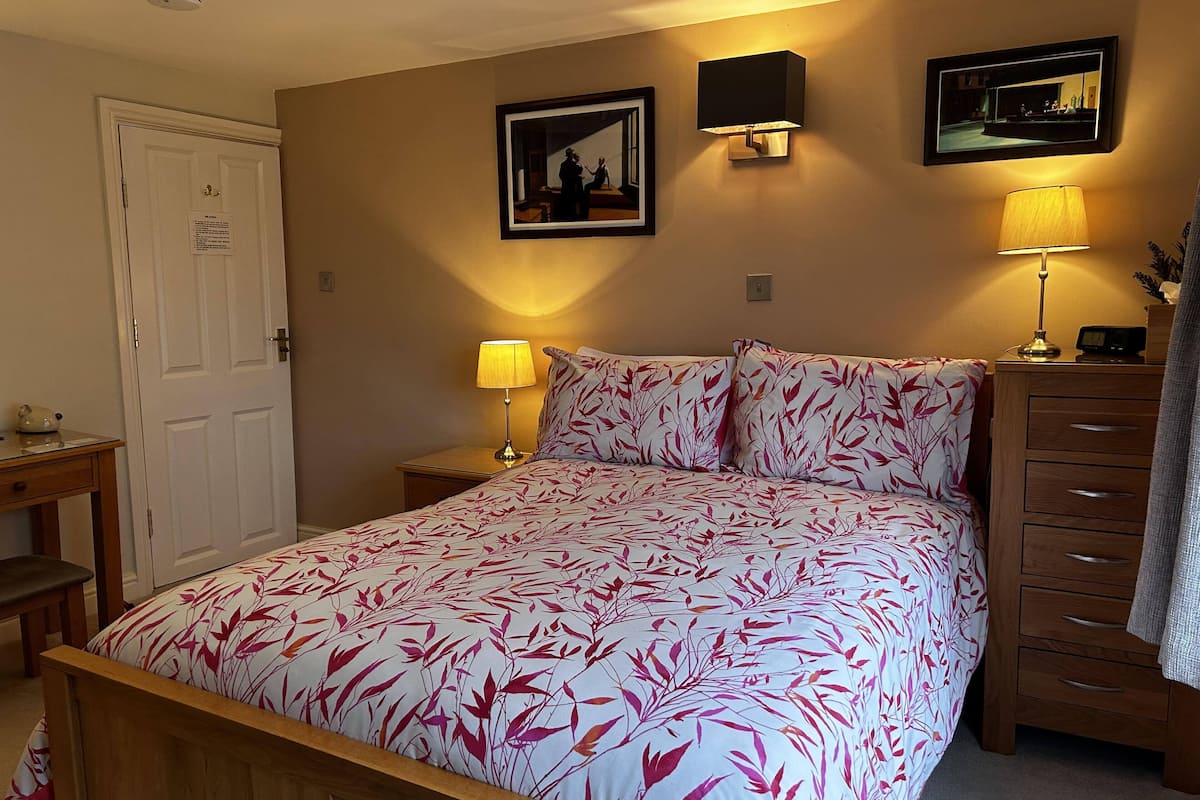 A bedroom with a bed, bedside tables, a dresser, and wall-mounted lamps.