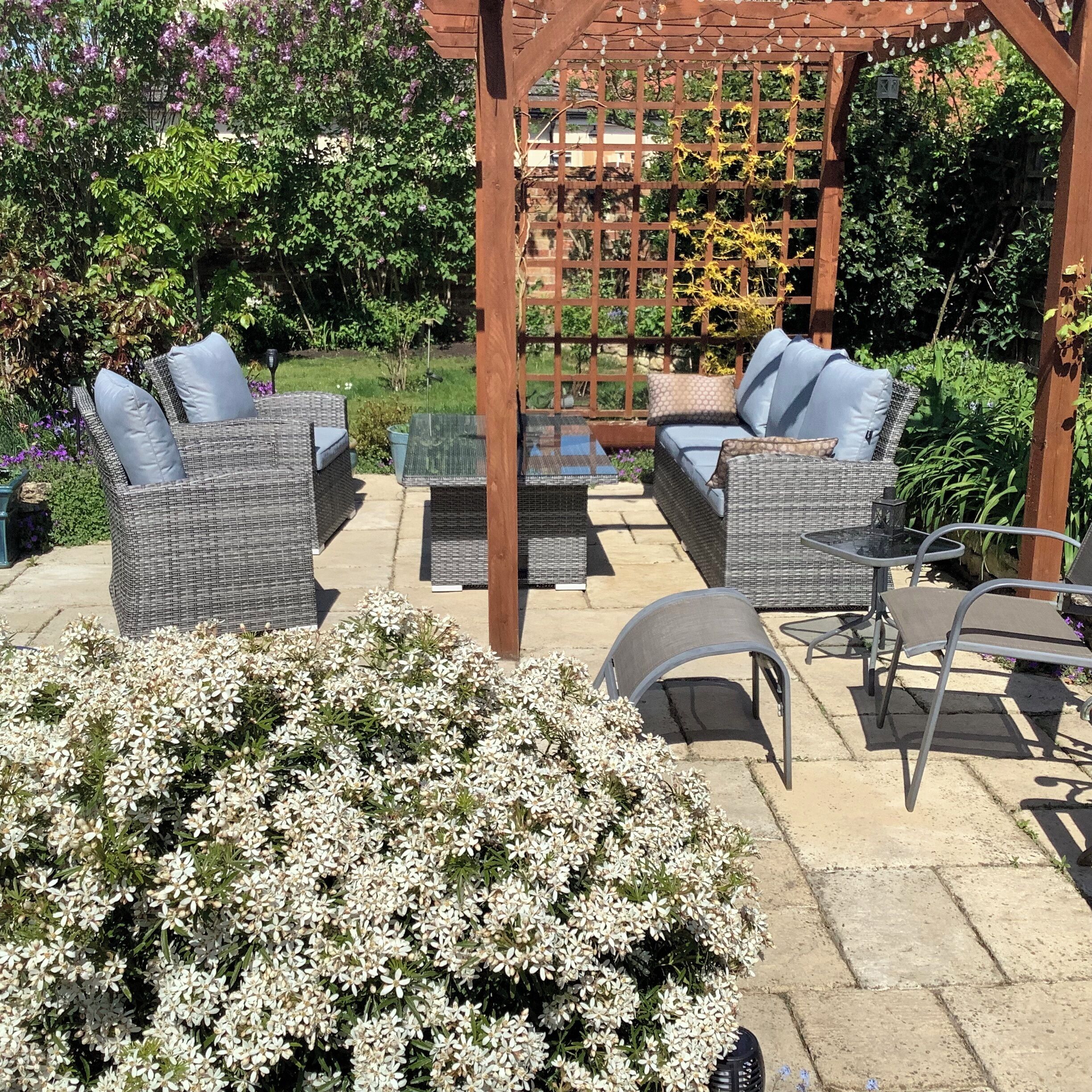 An outdoor patio with wicker furniture, a pergola, and a garden.