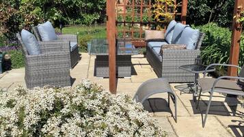 An outdoor patio with wicker furniture, a pergola, and a garden.