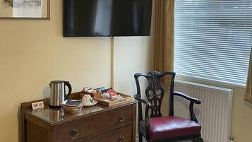 A room with a wooden dresser, a red leather chair, a flat-screen TV mounted on the wall, and a window with blinds.