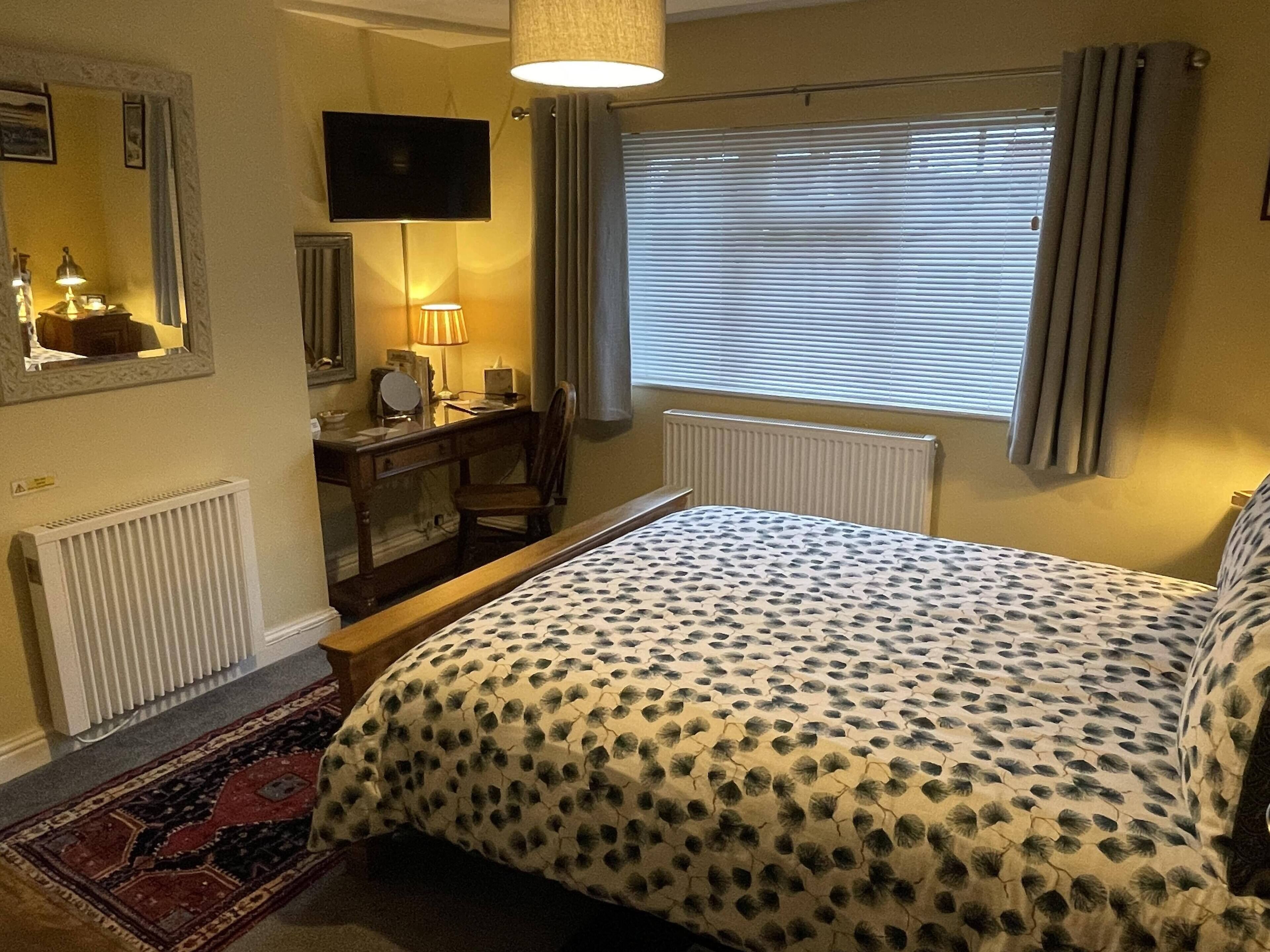 Ein Schlafzimmer mit einem Bett, einem Schreibtisch, einem Sessel, einem Fernseher und einem Fenster mit Vorhängen.