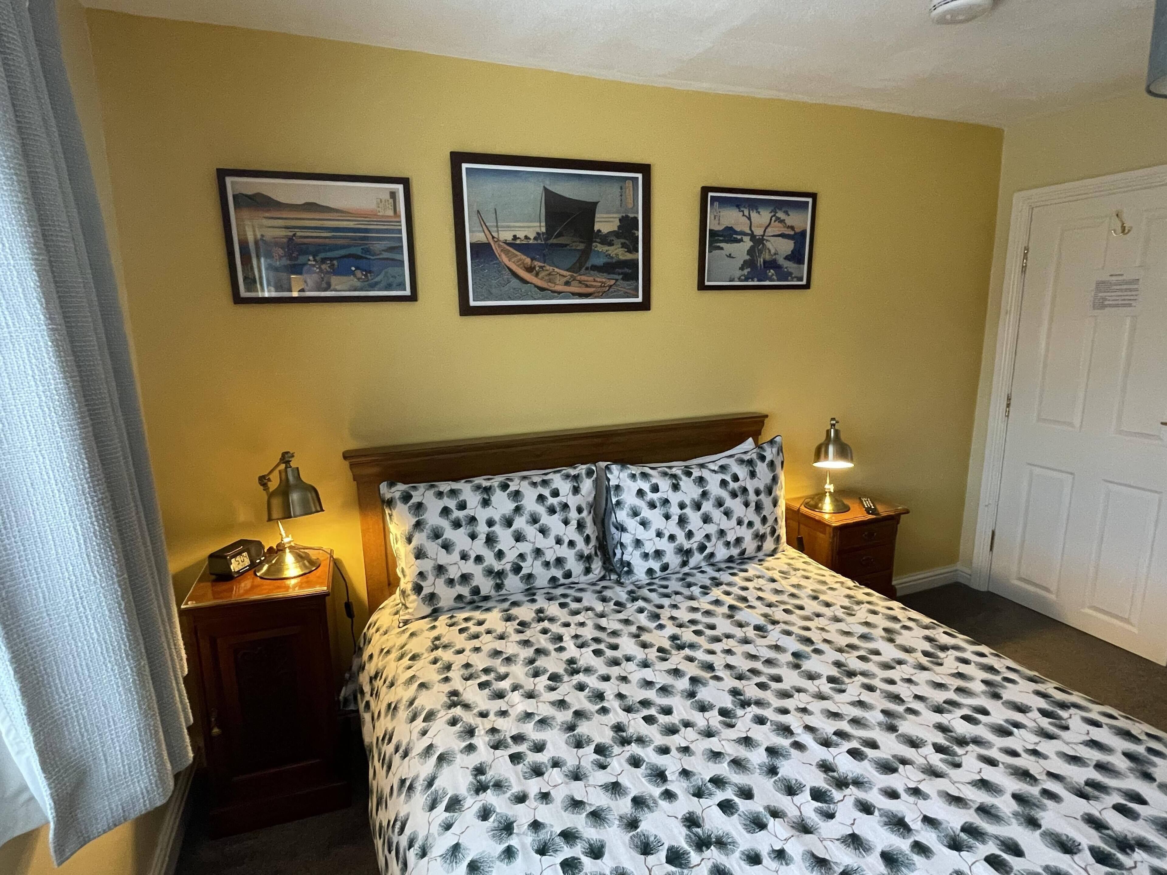 A hotel room with a bed, two bedside tables, a lamp, and three framed pictures on the wall.