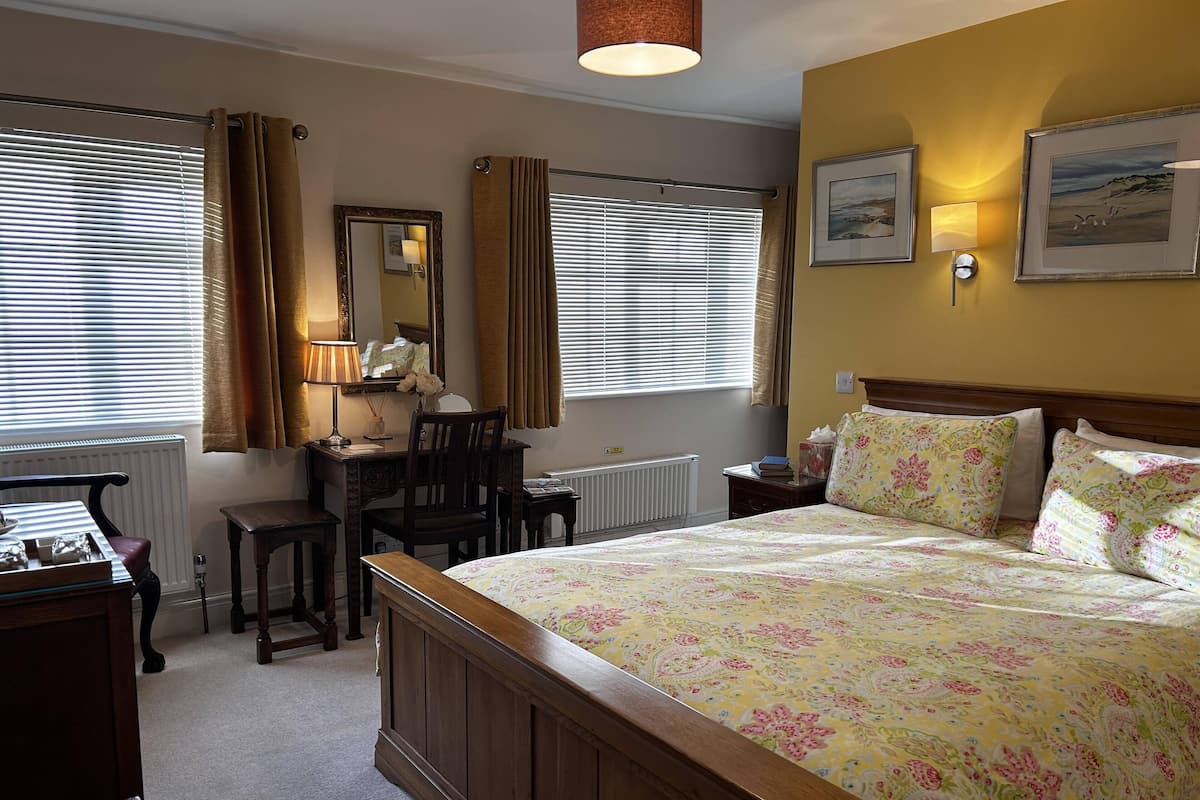 A bedroom with a large bed, a desk, a chair, and a radiator.