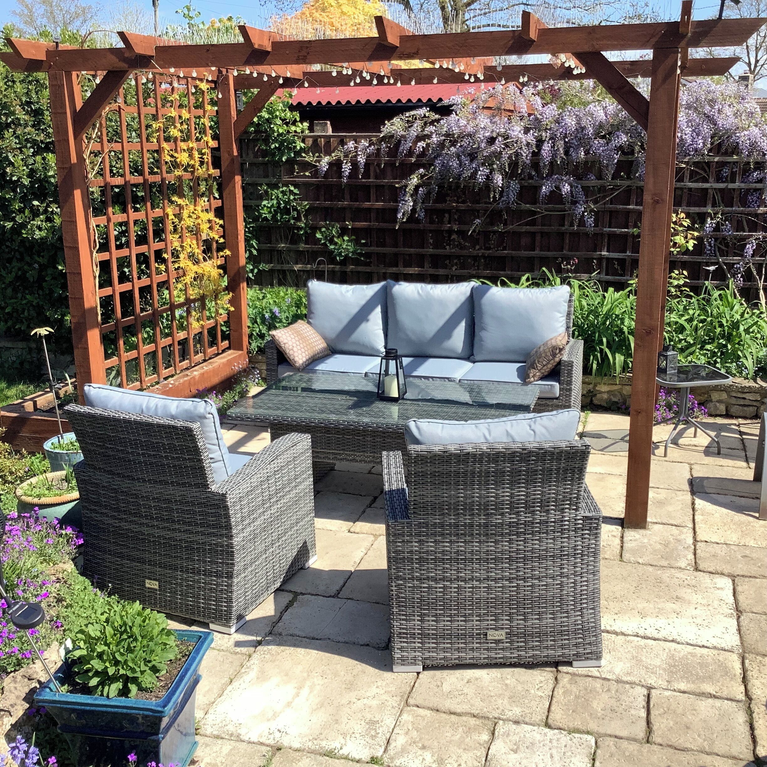Een terras met een houten pergola, rieten meubels en een tafel met glazen blad.