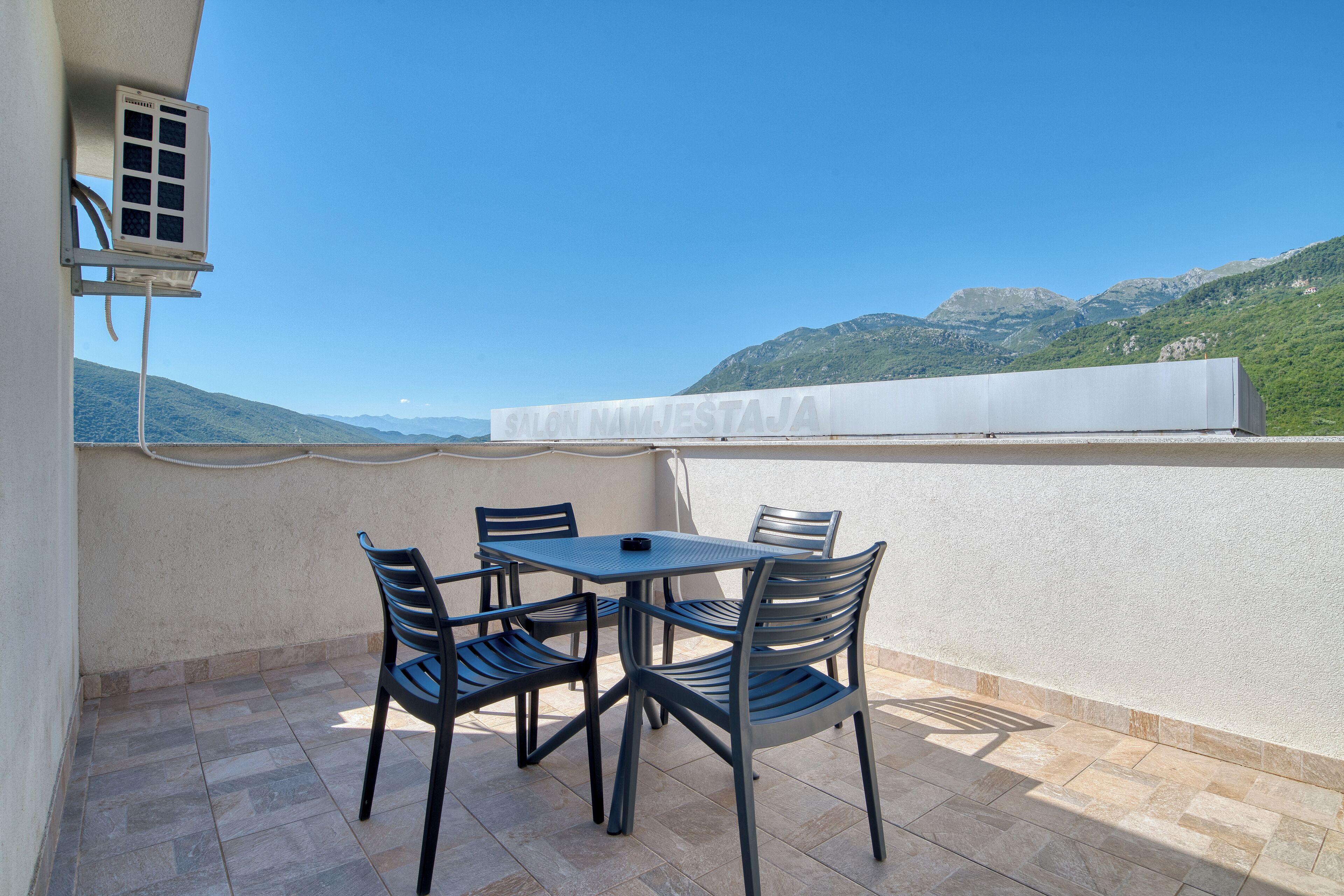 A terrace with a table and chairs, a white awning, and a view of mountains.