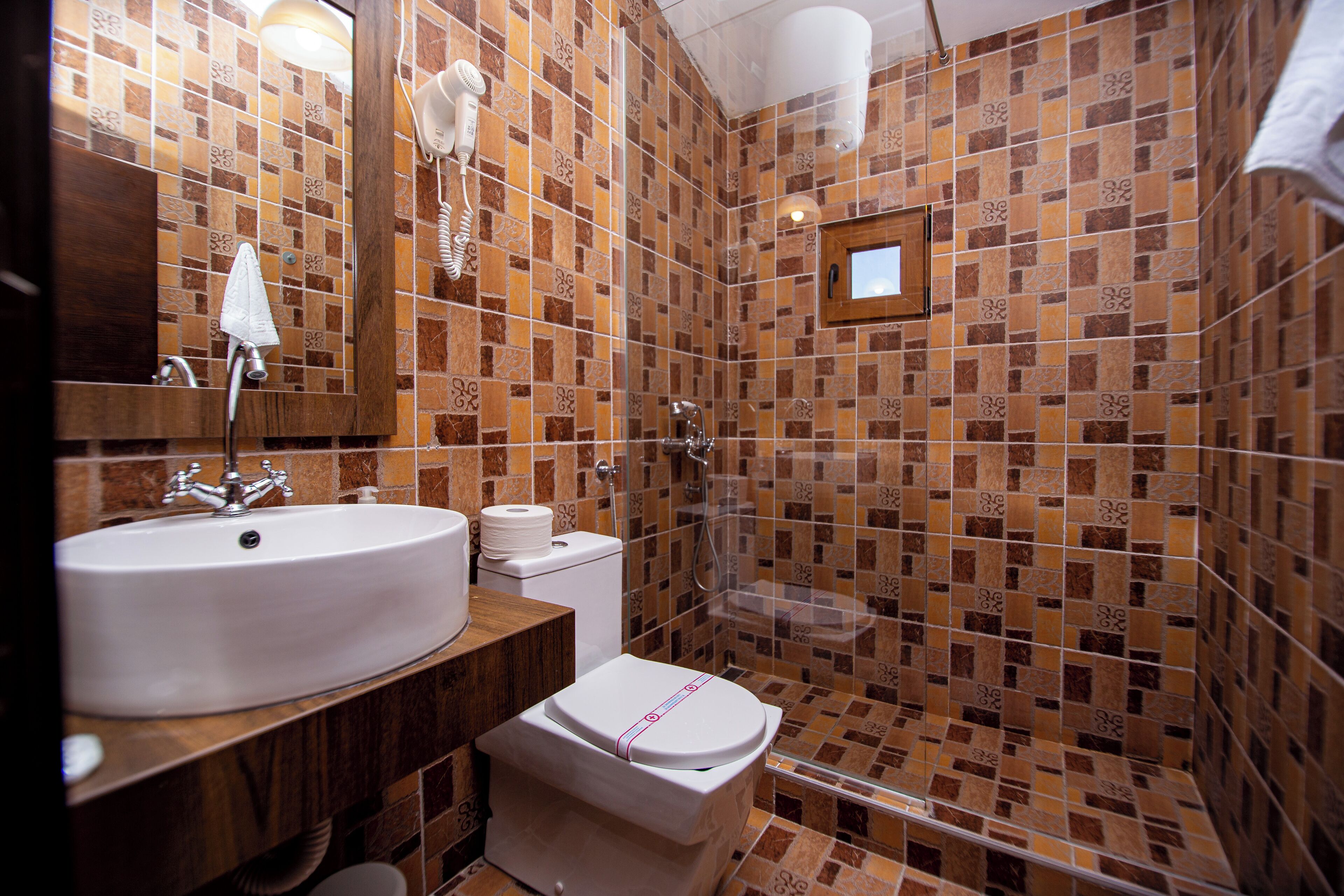 A bathroom with a sink, toilet, and shower area, featuring patterned tile walls and a wooden vanity.