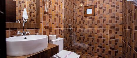 A bathroom with a sink, toilet, and shower area, featuring patterned tile walls and a wooden vanity.