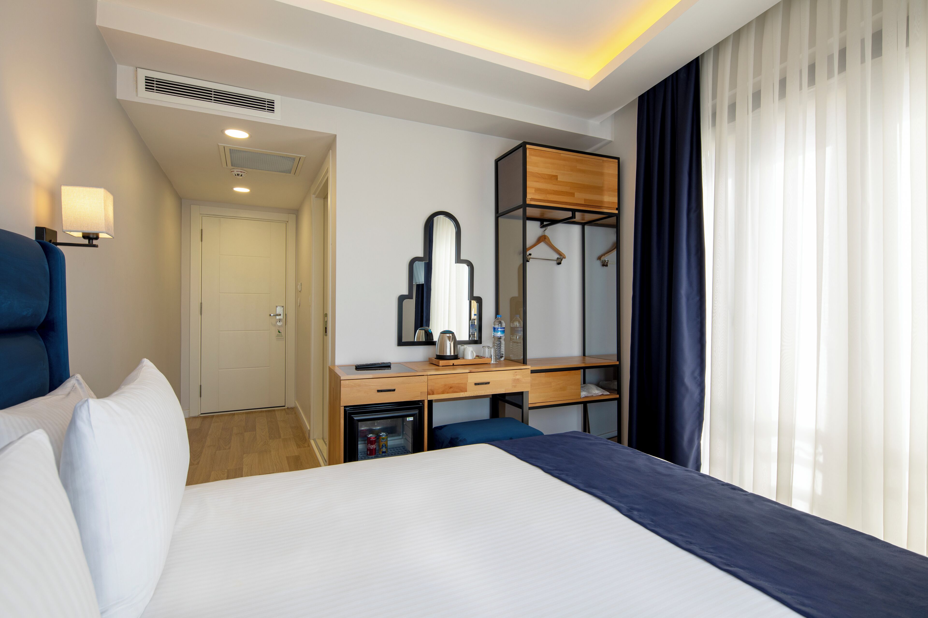 Una habitación de hotel con una cama, un escritorio con espejo, un armario y una ventana con cortinas.