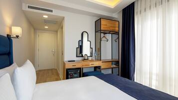 Una habitación de hotel con una cama, un escritorio con espejo, un armario y una ventana con cortinas.