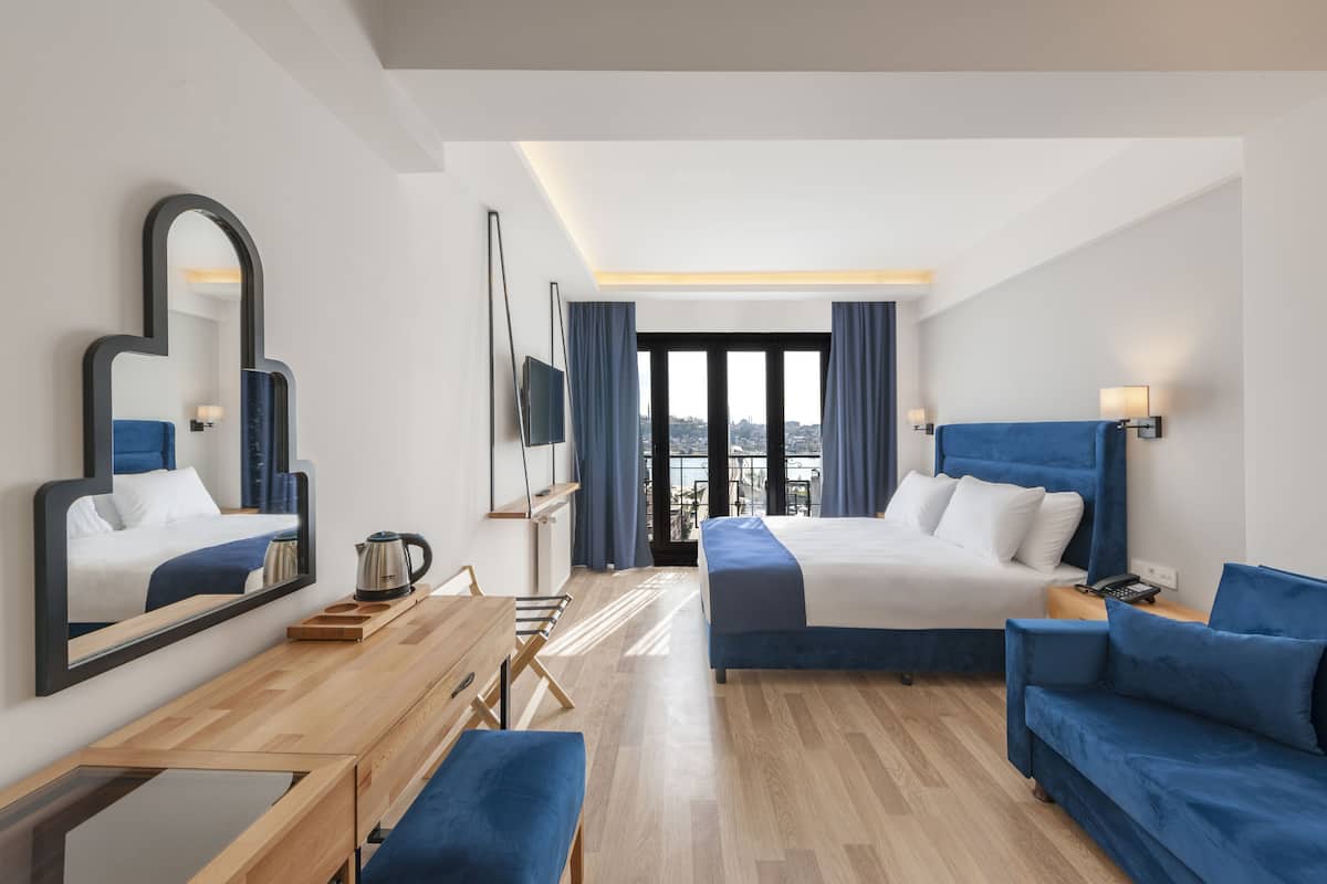 A modern hotel room with a large bed, a desk, a chair, a sofa, and a large mirror.