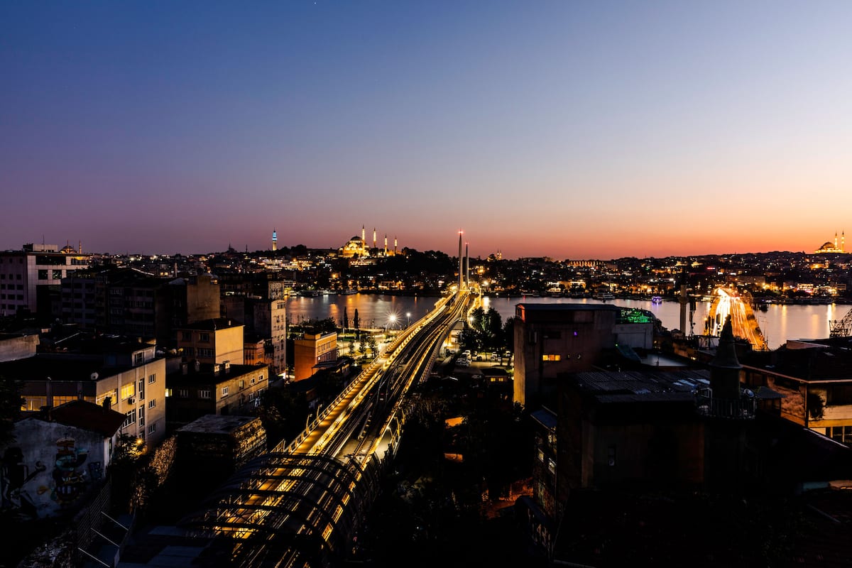 A nighttime cityscape with a prominent bridge, illuminated buildings, and a body of water.