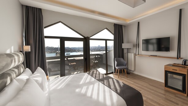 Een moderne hotelkamer met een groot bed, een televisie, een bureau en een balkon met uitzicht over de stad.