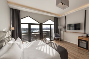 A modern hotel room with a large bed, a TV, a desk, and a balcony with a city view.