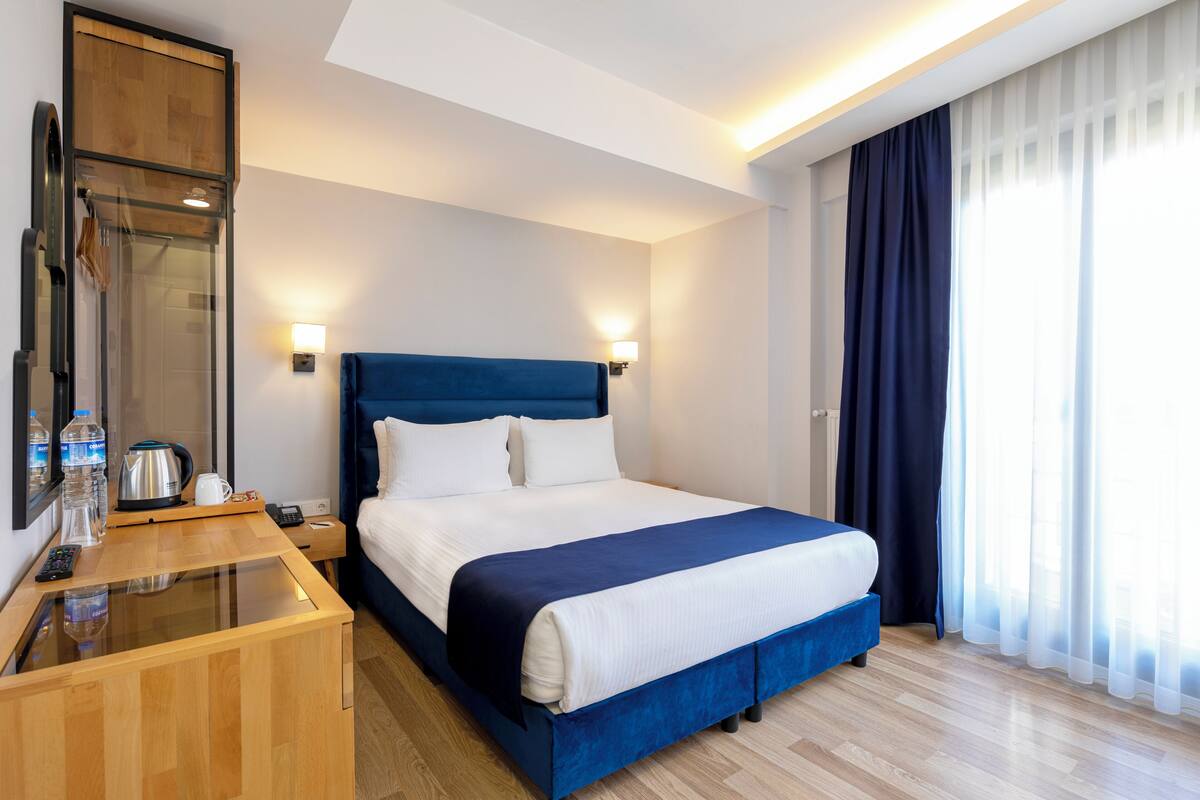 A hotel room with a bed, bedside table, and a large window with curtains.