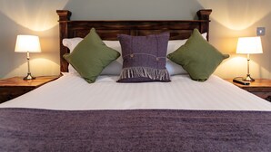 A neatly made bed with a wooden headboard, flanked by two bedside tables with lamps. - The Congresbury Arms (Bristol)