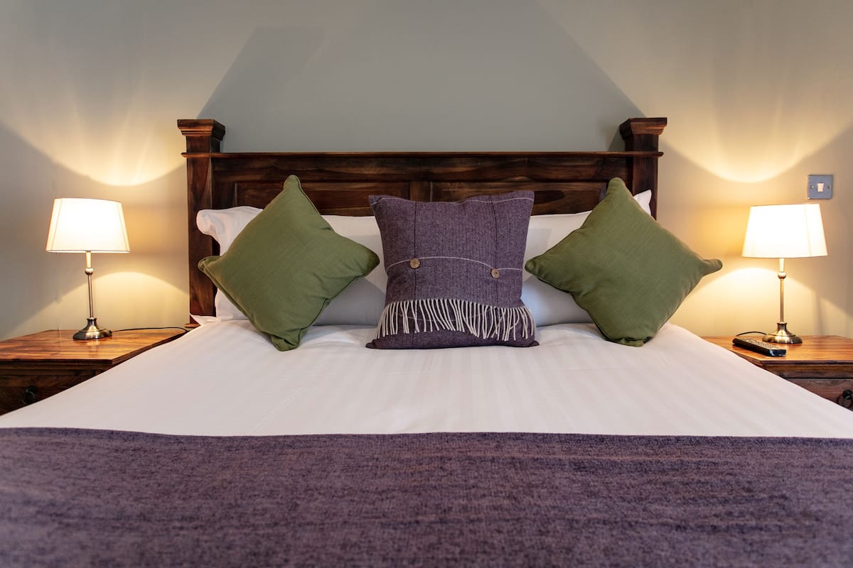 A neatly made bed with a wooden headboard, flanked by two bedside tables with lamps.