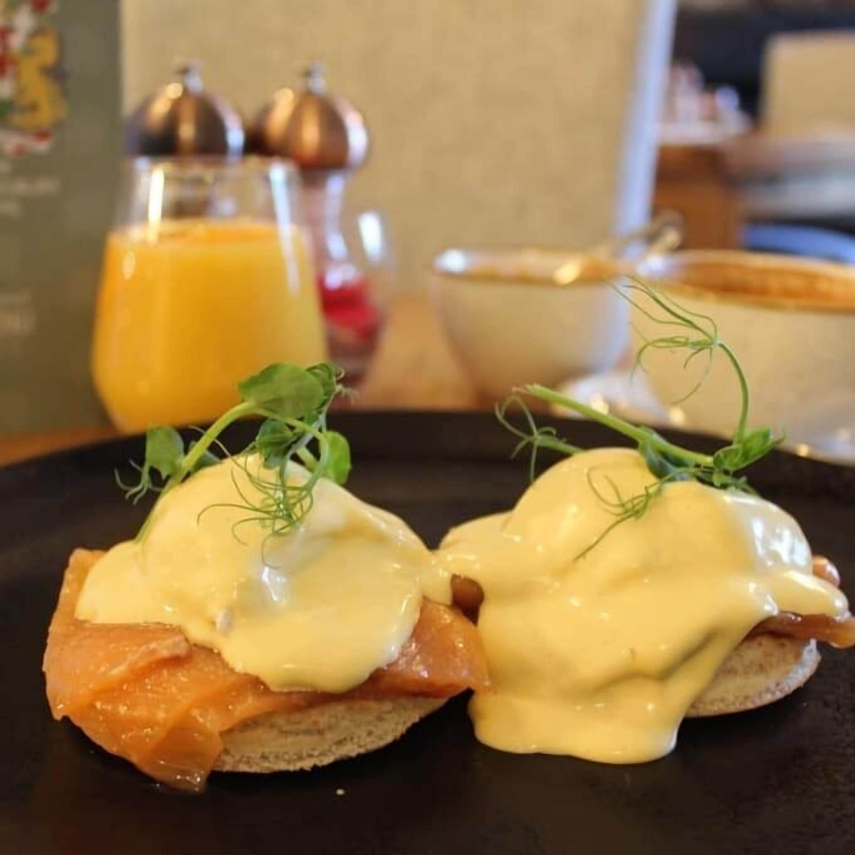 A breakfast setting with eggs Benedict on toast, a glass of orange juice, and a bowl of soup.