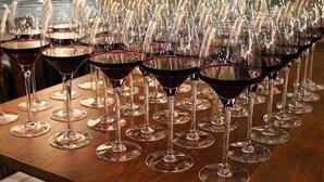 A table with numerous wine glasses filled with red wine, a hand pouring wine into one of the glasses, and a decorative wall in the background. - The Congresbury Arms (Bristol)