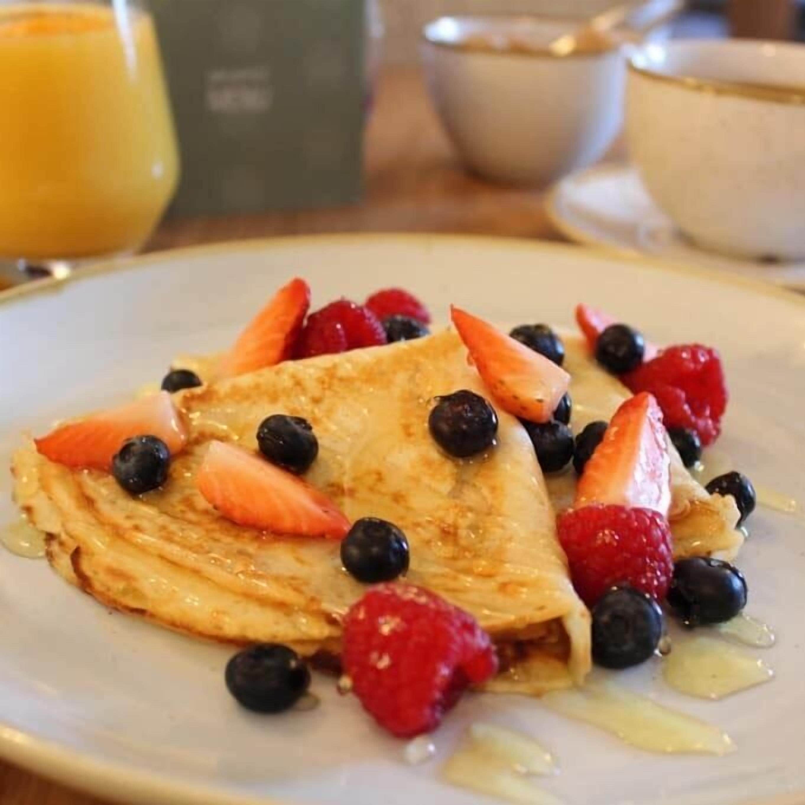 A plate with a folded crepe topped with strawberries, blueberries, and a drizzle of syrup.