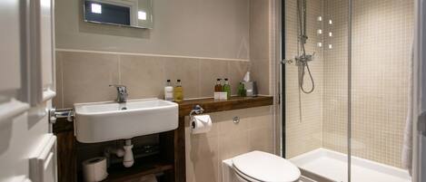 Un baño moderno con lavamanos, inodoro y ducha con mampara de vidrio.